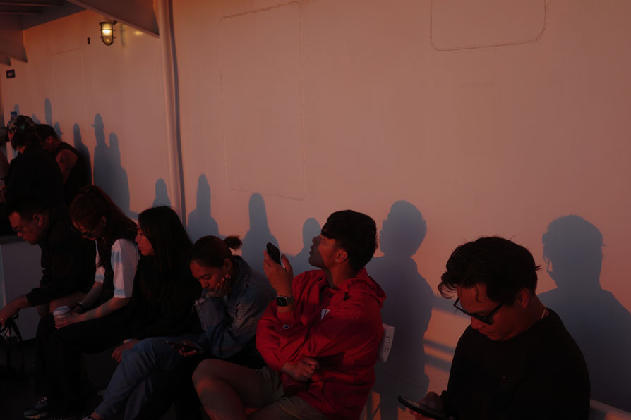 Photo shows a row of peopls seated against the wall on a ferry at dusk,
	reddish light and shadows cast on the wall.
